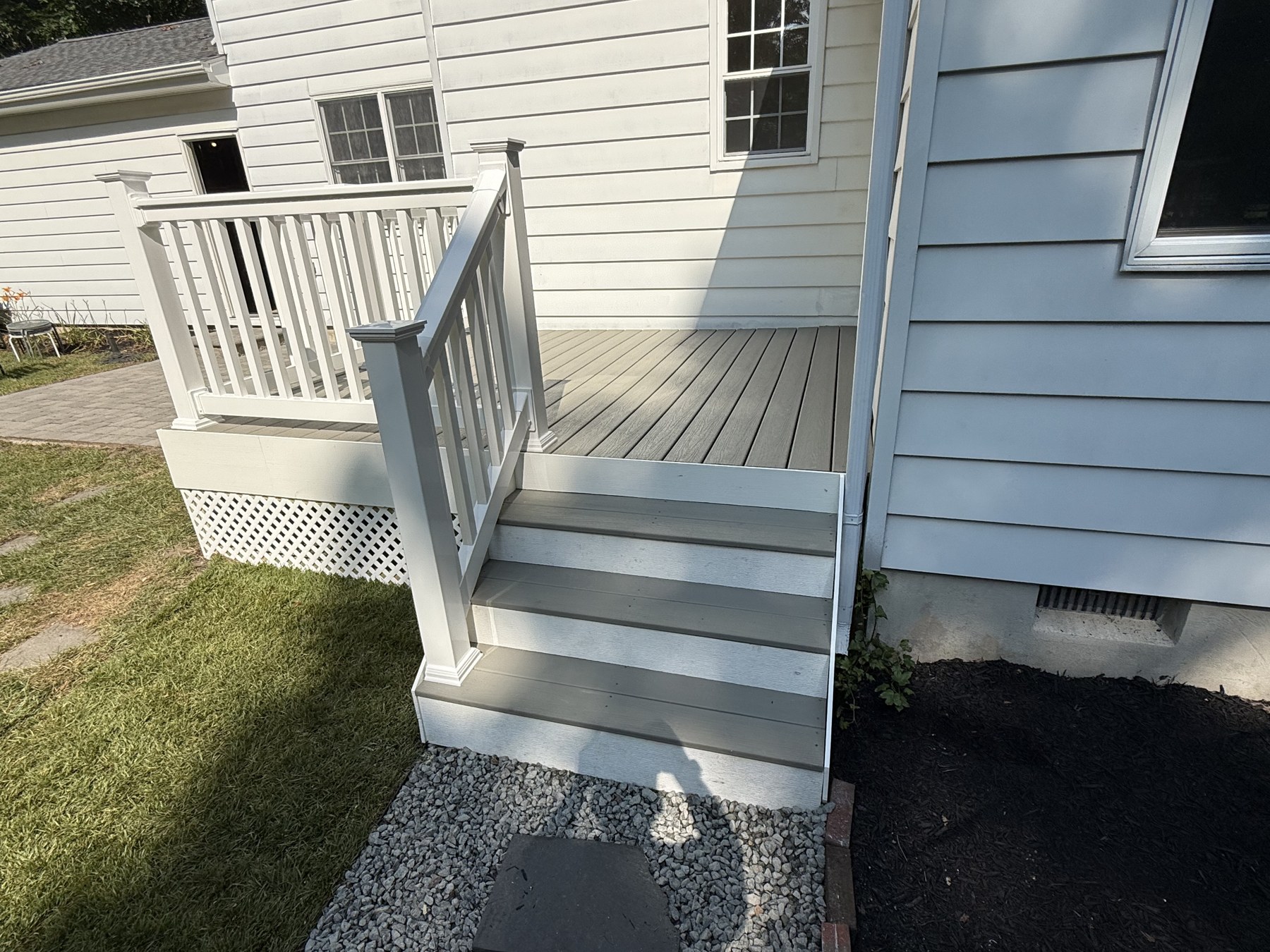 Finished composite deck steps with a white handrail and lattice skirting in Medford